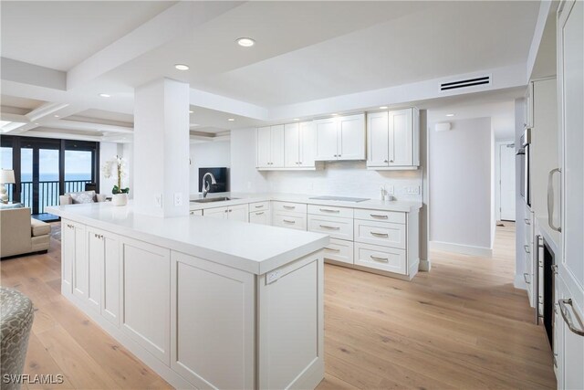 kitchen featuring kitchen peninsula, light hardwood / wood-style flooring, coffered ceiling, and backsplash