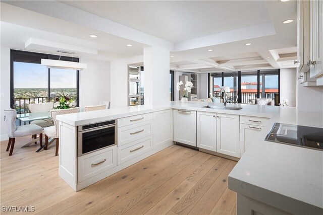 kitchen with coffered ceiling, stainless steel oven, light wood-type flooring, sink, and kitchen peninsula