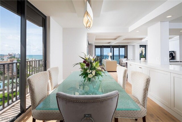 dining room featuring light wood-style flooring, coffered ceiling, a water view, beam ceiling, and a view of city