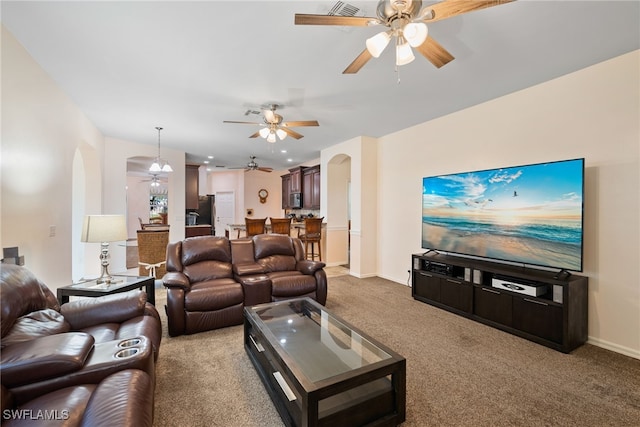 living area with arched walkways, light carpet, ceiling fan, and baseboards