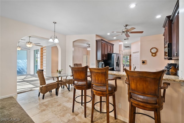 kitchen with a healthy amount of sunlight, light stone countertops, arched walkways, and stainless steel refrigerator with ice dispenser