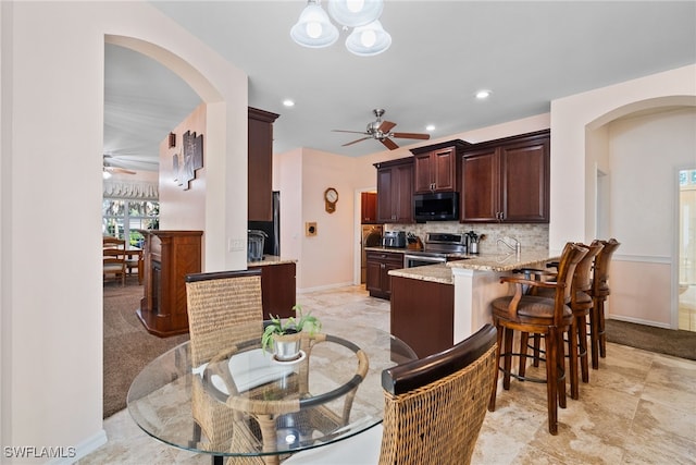 kitchen with backsplash, a ceiling fan, light stone countertops, stainless steel range with electric stovetop, and a peninsula