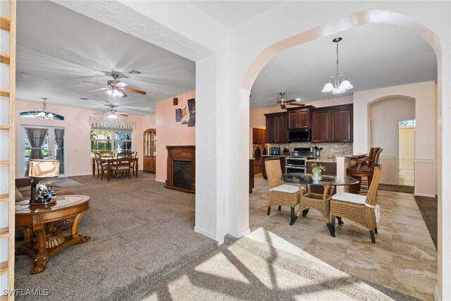 dining area featuring ceiling fan with notable chandelier, arched walkways, and a glass covered fireplace