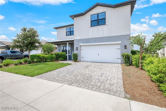 view of front of home with decorative driveway, stucco siding, an attached garage, board and batten siding, and a front lawn