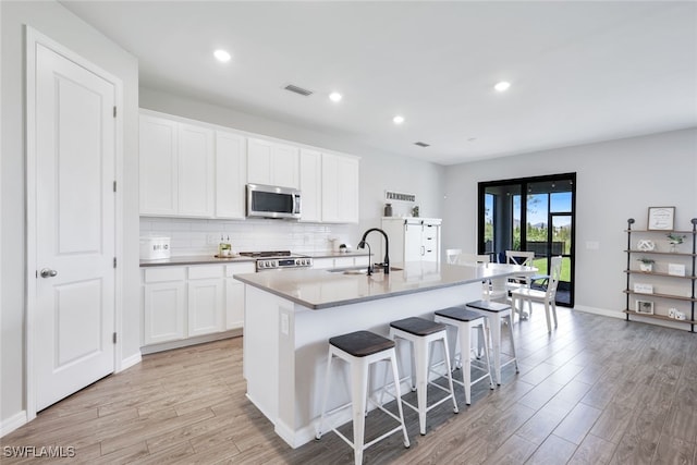 kitchen with a kitchen island with sink, white cabinets, and stainless steel microwave