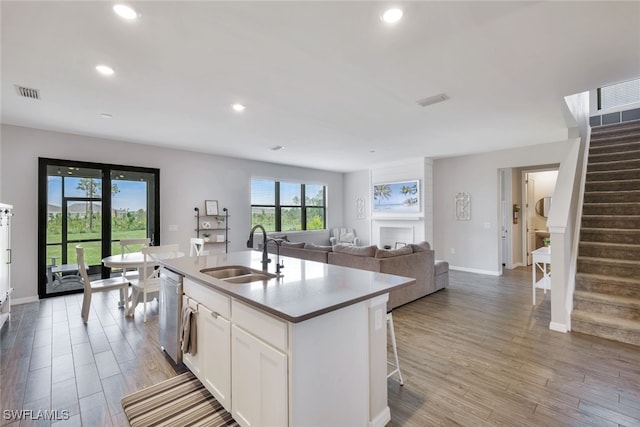 kitchen featuring a sink, visible vents, white cabinets, open floor plan, and a center island with sink