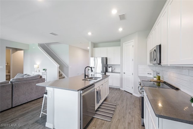 kitchen with a kitchen island with sink, light wood-style floors, open floor plan, white cabinets, and appliances with stainless steel finishes