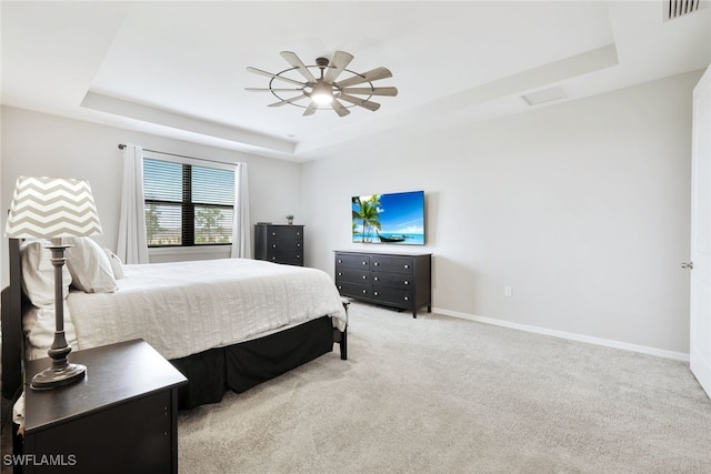 bedroom with a tray ceiling, visible vents, light carpet, and baseboards