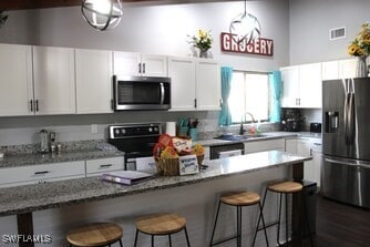 kitchen with a breakfast bar area, stainless steel appliances, white cabinetry, and a sink