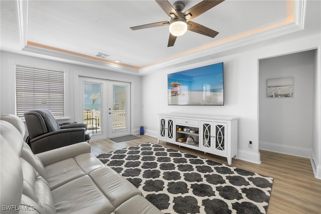 living room featuring french doors, ornamental molding, light hardwood / wood-style floors, and a tray ceiling