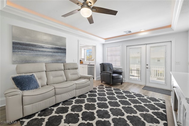 living room with ornamental molding, ceiling fan, light hardwood / wood-style floors, a raised ceiling, and french doors