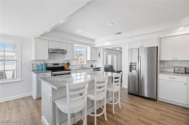 kitchen featuring appliances with stainless steel finishes, white cabinetry, sink, a center island, and light stone counters