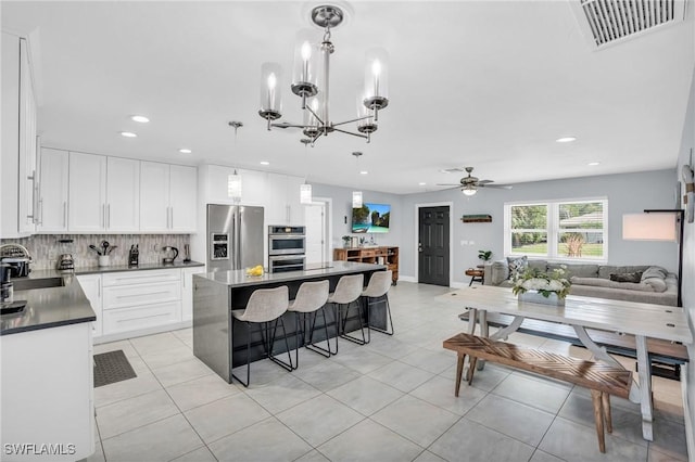 kitchen featuring hanging light fixtures, stainless steel appliances, white cabinets, a kitchen island, and decorative backsplash