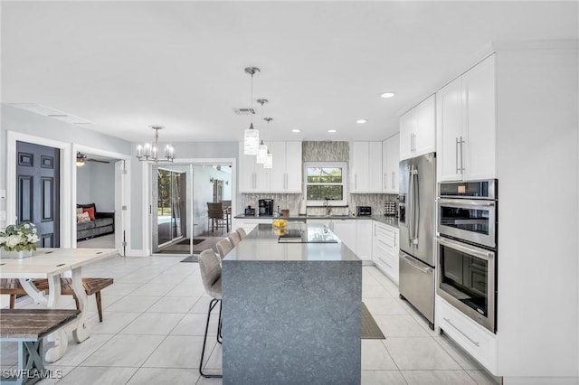 kitchen with light tile patterned flooring, white cabinetry, appliances with stainless steel finishes, a kitchen island, and pendant lighting