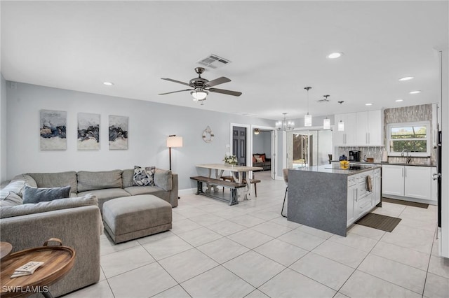 living room featuring light tile patterned flooring, sink, and ceiling fan with notable chandelier