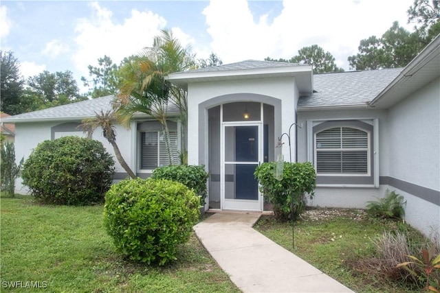 entrance to property featuring a shingled roof, a lawn, and stucco siding