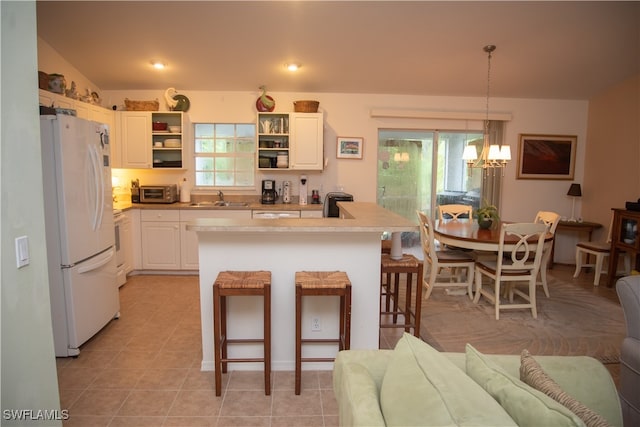 kitchen with a breakfast bar area, an inviting chandelier, hanging light fixtures, a center island with sink, and white refrigerator