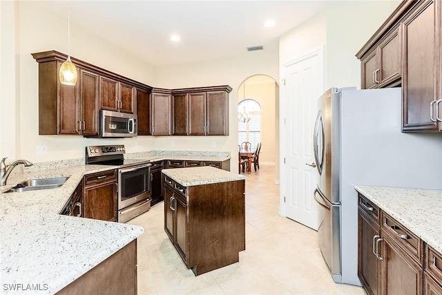 kitchen with arched walkways, light stone counters, appliances with stainless steel finishes, hanging light fixtures, and a sink