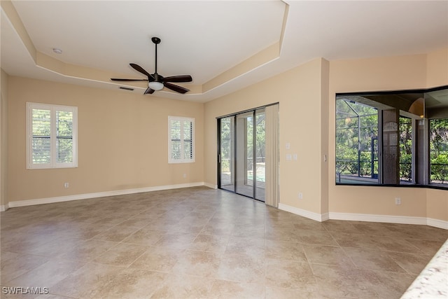 spare room with a tray ceiling, ceiling fan, and light tile patterned floors