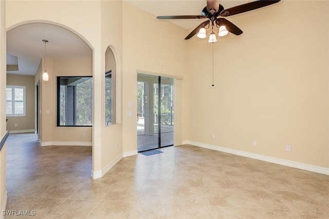 spare room with light tile patterned floors, baseboards, arched walkways, a ceiling fan, and a towering ceiling