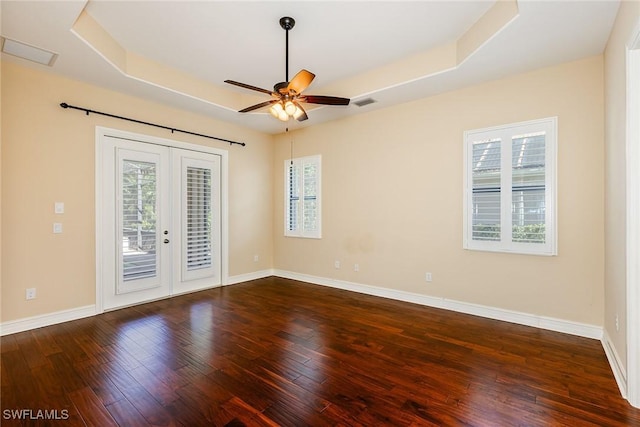 empty room featuring dark wood-style floors, a tray ceiling, a wealth of natural light, and french doors