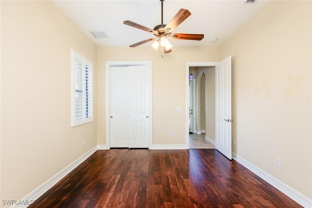 unfurnished bedroom with dark wood-style flooring, a ceiling fan, visible vents, baseboards, and a closet