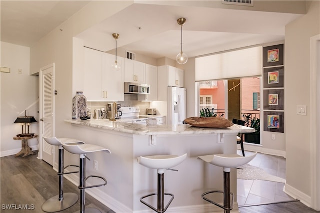 kitchen with a breakfast bar area, kitchen peninsula, white appliances, and white cabinets