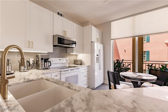 kitchen with light stone countertops, tasteful backsplash, white appliances, and white cabinets