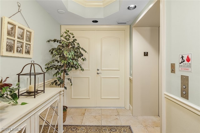 entrance foyer with light tile patterned floors, ornamental molding, and a tray ceiling