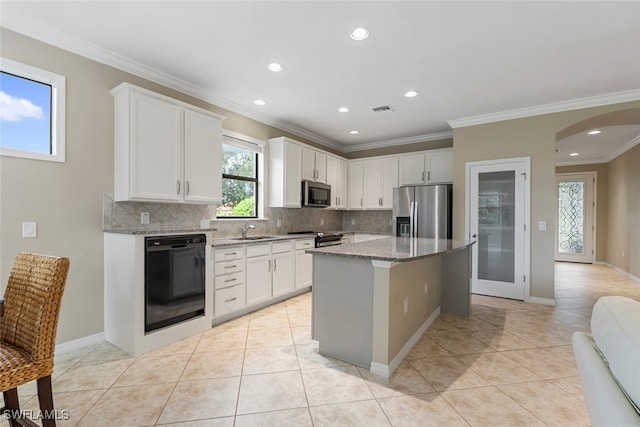 kitchen featuring appliances with stainless steel finishes, tasteful backsplash, light stone counters, a kitchen island, and white cabinetry