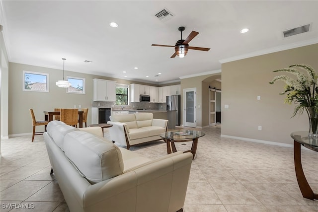 living room with a barn door, ceiling fan, light tile patterned floors, and ornamental molding