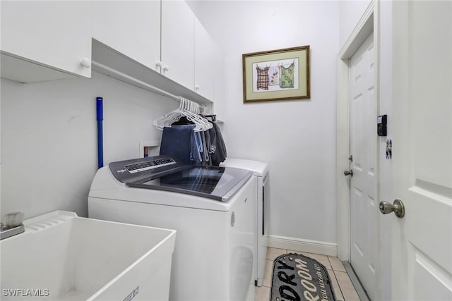 clothes washing area with light tile patterned flooring, washing machine and dryer, cabinets, and sink