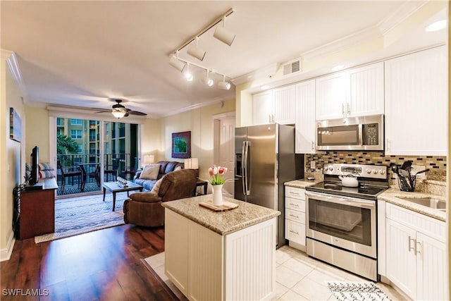 kitchen with white cabinets, stainless steel appliances, crown molding, and light hardwood / wood-style floors