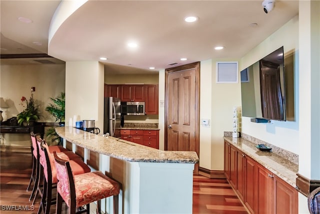 kitchen with hardwood / wood-style flooring, appliances with stainless steel finishes, light stone counters, kitchen peninsula, and a breakfast bar area