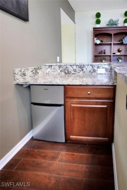 interior space with refrigerator, light stone counters, and dark wood-type flooring