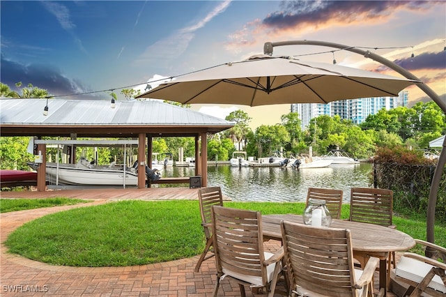 patio terrace at dusk featuring a water view and a lawn