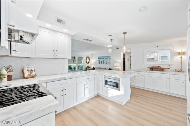 kitchen featuring stainless steel microwave, kitchen peninsula, white cabinets, range hood, and backsplash