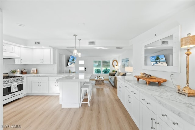 kitchen featuring stainless steel stove, white cabinets, a kitchen bar, hanging light fixtures, and light hardwood / wood-style flooring