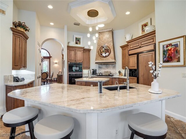 kitchen with sink, a breakfast bar, a tray ceiling, light stone countertops, and a large island with sink