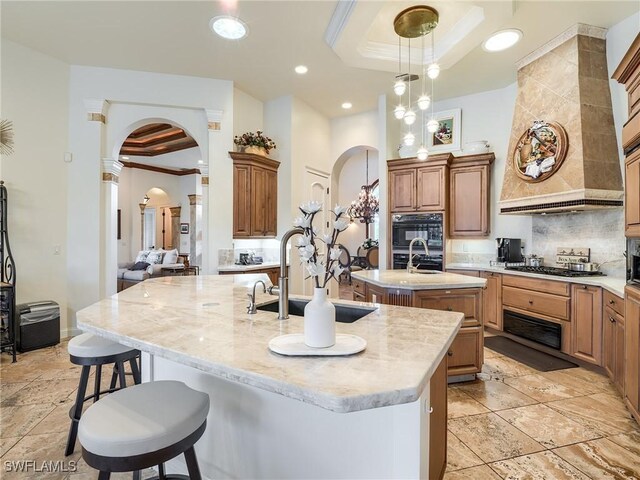 kitchen featuring sink, ornamental molding, a raised ceiling, and a center island with sink