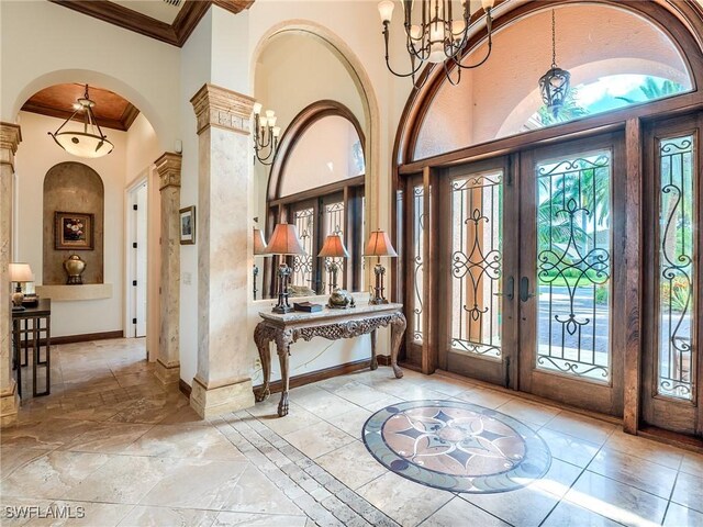 foyer entrance featuring an inviting chandelier, a towering ceiling, ornamental molding, and french doors