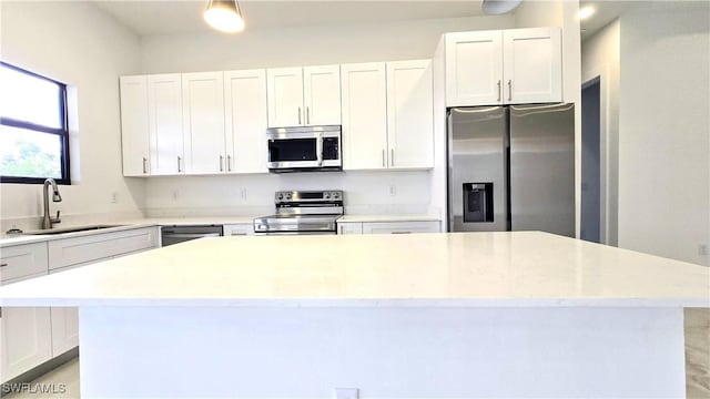 kitchen with appliances with stainless steel finishes, sink, white cabinets, and a center island