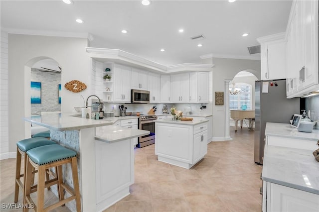 kitchen featuring arched walkways, a peninsula, stainless steel appliances, white cabinetry, and open shelves