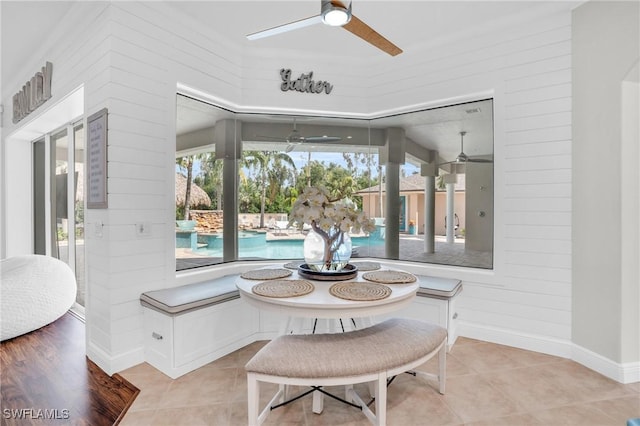 dining area with ceiling fan, wood walls, and light tile patterned flooring