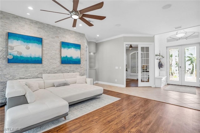 living area featuring an accent wall, wood finished floors, a ceiling fan, ornamental molding, and french doors