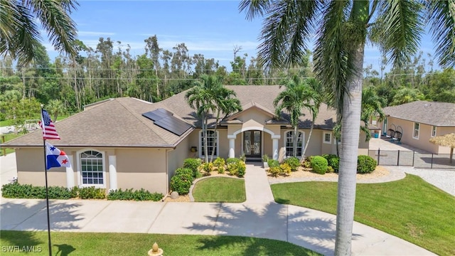 view of front facade with solar panels, fence, roof with shingles, stucco siding, and a front yard