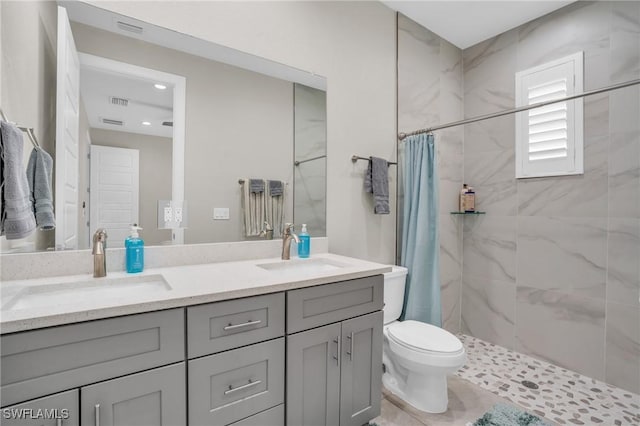 full bath featuring double vanity, toilet, a tile shower, and a sink