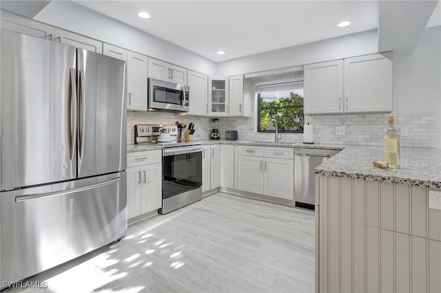 kitchen with light stone counters, white cabinets, appliances with stainless steel finishes, and sink