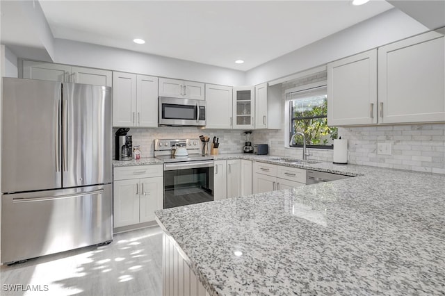 kitchen with stainless steel appliances, a sink, light stone countertops, tasteful backsplash, and glass insert cabinets