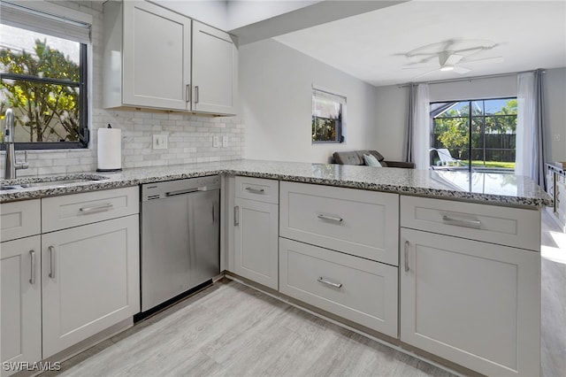 kitchen featuring light stone counters, a sink, light wood finished floors, dishwasher, and tasteful backsplash